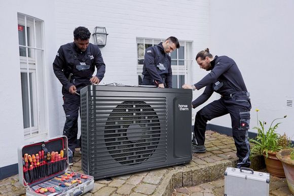 Drei Personen montieren eine Wärmepumpe.